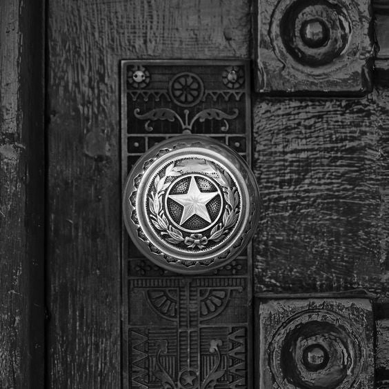 Black and white photograph of a brass lone star door knob on a door leading into the Texas State Capitol Building in Austin. (Square format)  This is one of the well-worn door knobs leading into the magnificent Texas state capitol building in Austin. Imagine how many interesting characters from Texas history must have touched this knob, and how many scoundrels!